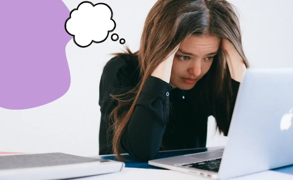 Uma mulher, com as mãos na cabeça, olha para um laptop com uma expressão de preocupação. Uma nuvem de pensamento vazia paira sobre sua cabeça.