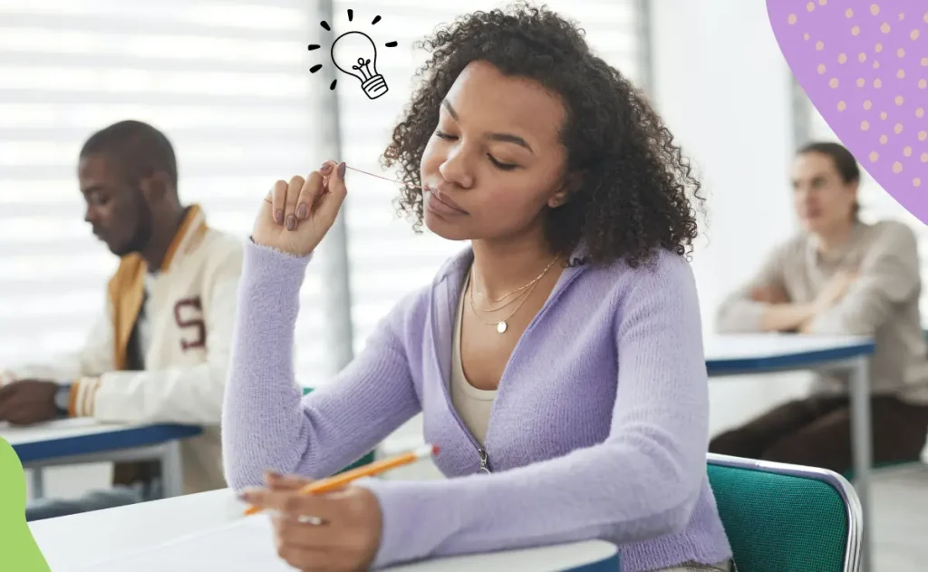 Uma mulher com cabelos cacheados e uma blusa roxa, sentada em uma carteira escolar, pensa com uma lâmpada desenhada acima de sua cabeça. Ao seu lado, outros estudantes estudam em uma sala de aula.