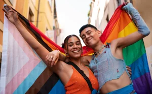 Duas pessoas sorrindo felizes com bandeiras do orgulho LGBT, celebrando o dia internacional do orgulho LGBT em uma rua urbana.