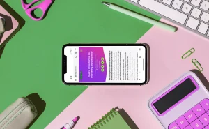 Imagem de um celular exibindo conteúdo sobre ferramentas tecnológicas para gestão escolar, rodeado de itens de escritório como caneta, tesoura, calculadora e teclado, em um ambiente organizado e colorido.