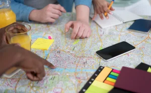 Estudantes discutindo estratégias para usar o Estatuto das Cidades na redação do Enem durante uma reunião com mapa, blocos de notas e celulares.