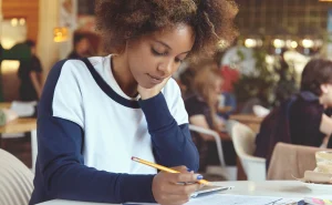 Jovem estudante usando repertório crítico na redação, com foco na leitura e compreensão, em ambiente de cafeteria ou biblioteca, demonstrando atenção ao trabalho escolar, contribuindo para uma redação argumentativa eficiente.