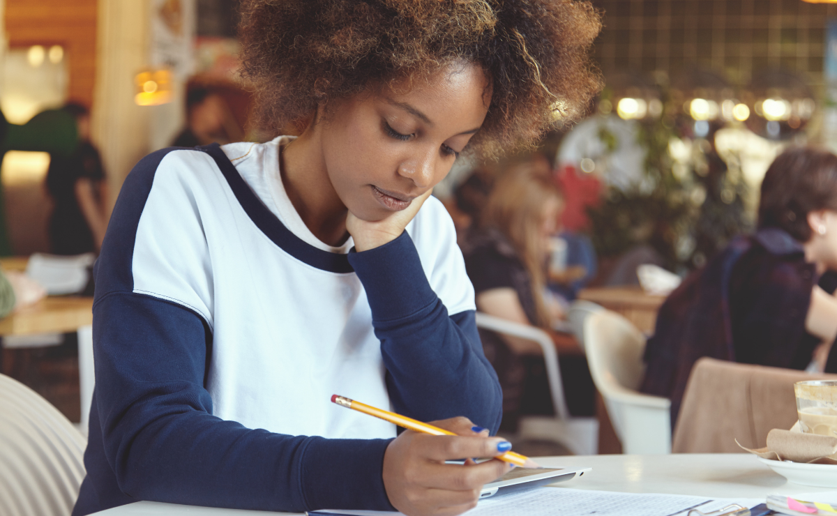 Jovem estudante usando repertório crítico na redação, com foco na leitura e compreensão, em ambiente de cafeteria ou biblioteca, demonstrando atenção ao trabalho escolar, contribuindo para uma redação argumentativa eficiente.