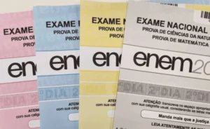 Quatro cadernos de provas do ENEM (Exame Nacional do Ensino Médio) empilhados, mostrando as capas coloridas em rosa, azul claro, amarelo e o primeiro caderno em tons de bege