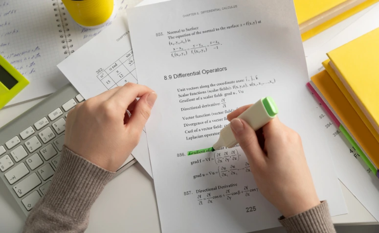 Mãos de um estudante usando marca-texto em uma folha de cálculo e equações matemáticas, simbolizando a preparação e a expectativa pela nota do ENEM 2025.